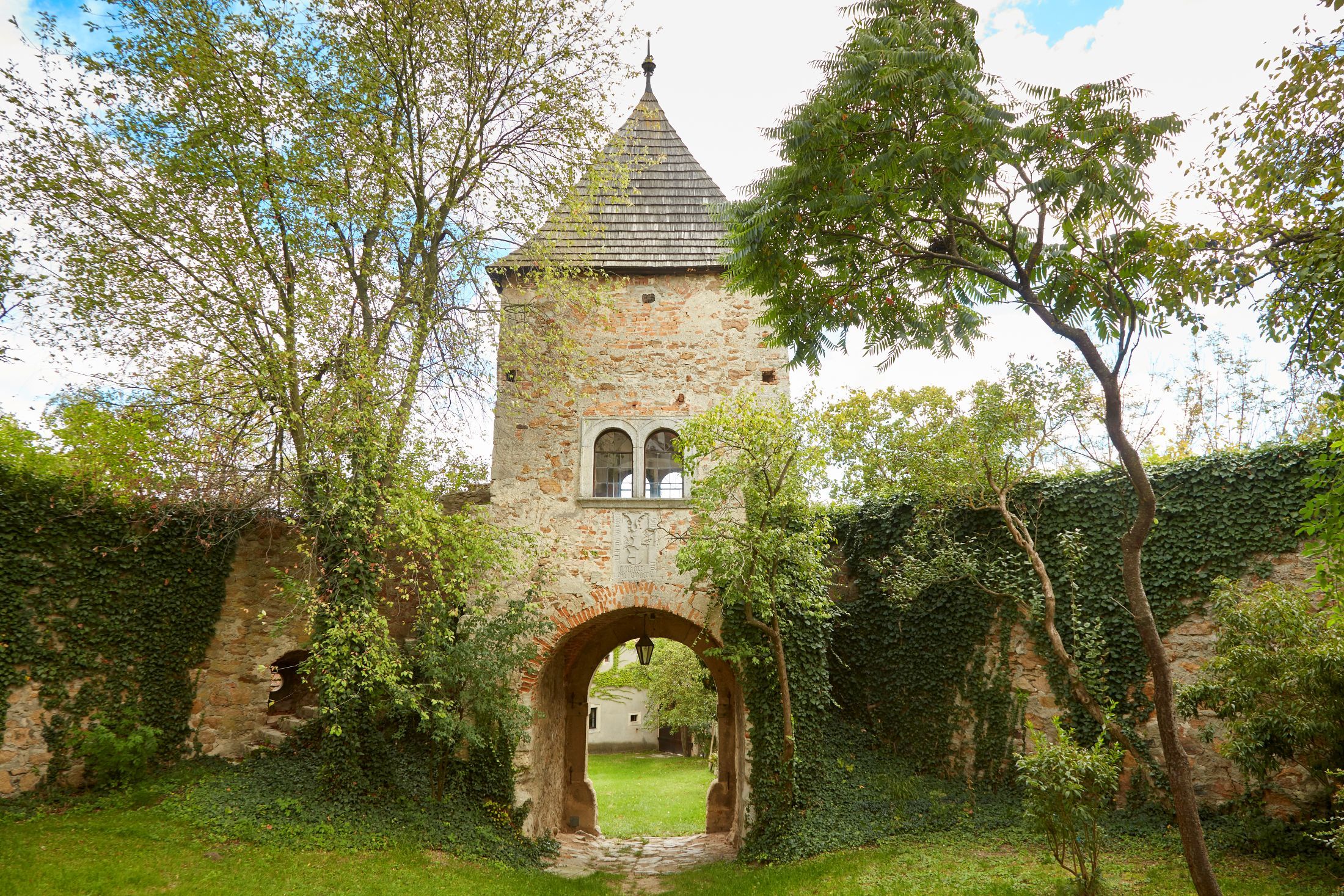 A medieval castle tower with an archway, surrounded by trees and ivy-covered walls.