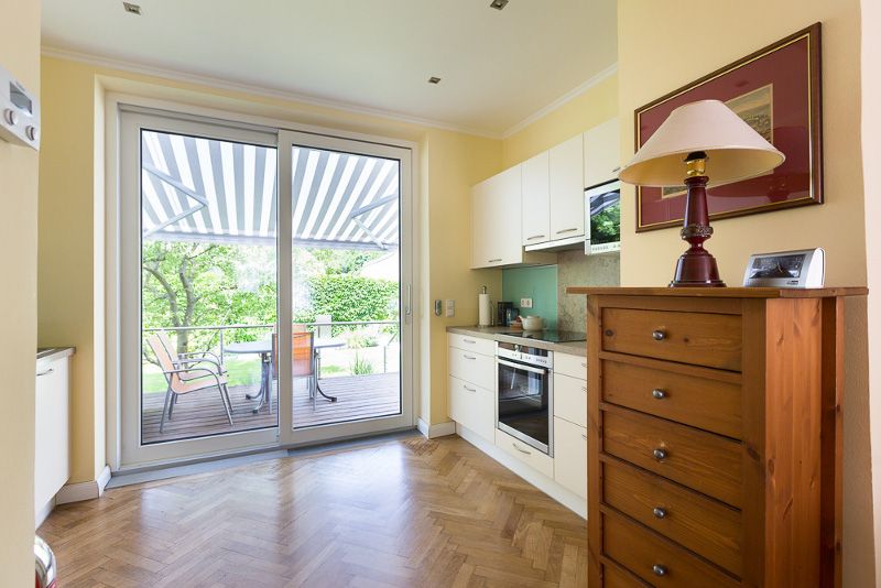 Bright kitchen with parquet floor, cupboard, stove and large glass door to the terrace with awning.