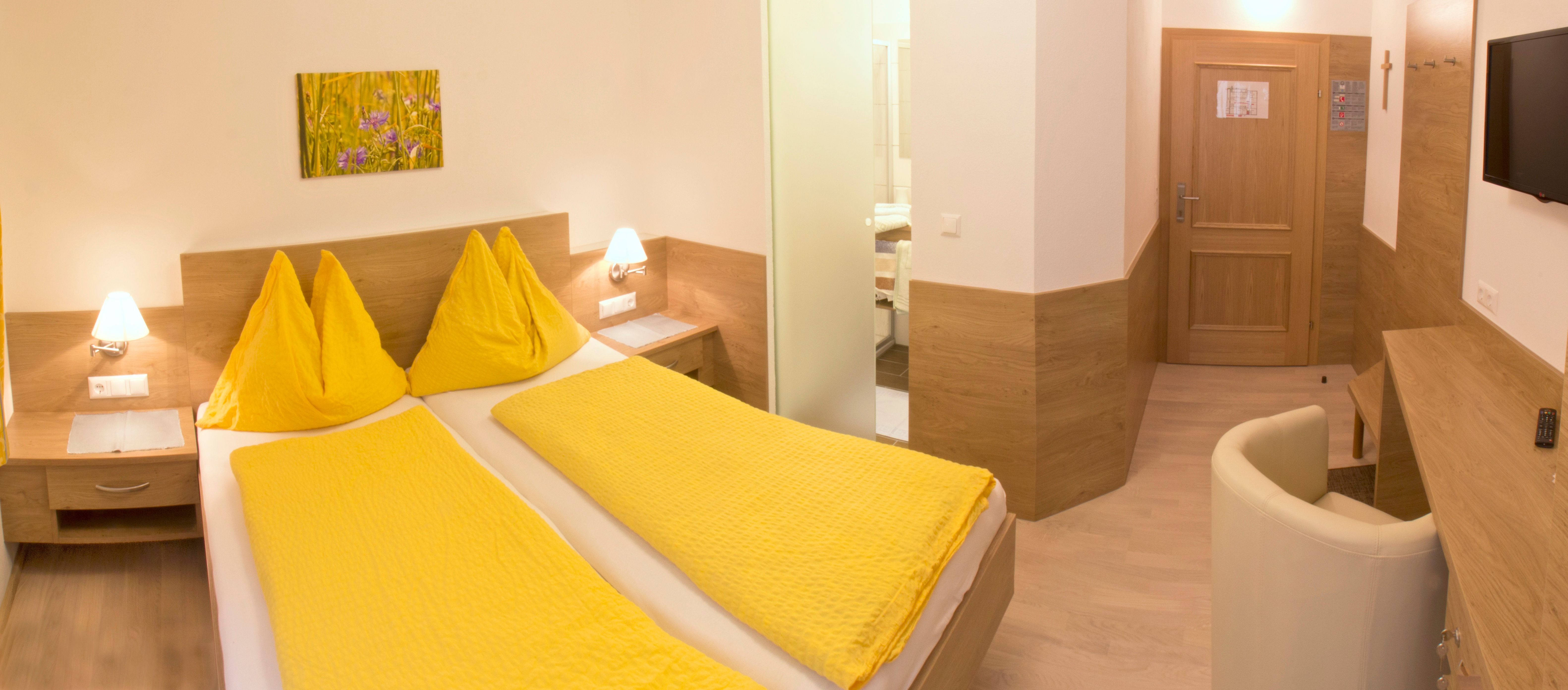 Hotel room with yellow bed linen, wooden furniture and a picture on the wall.