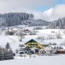 Winter landscape with snow-covered Café Pension Kristall and surrounding houses.