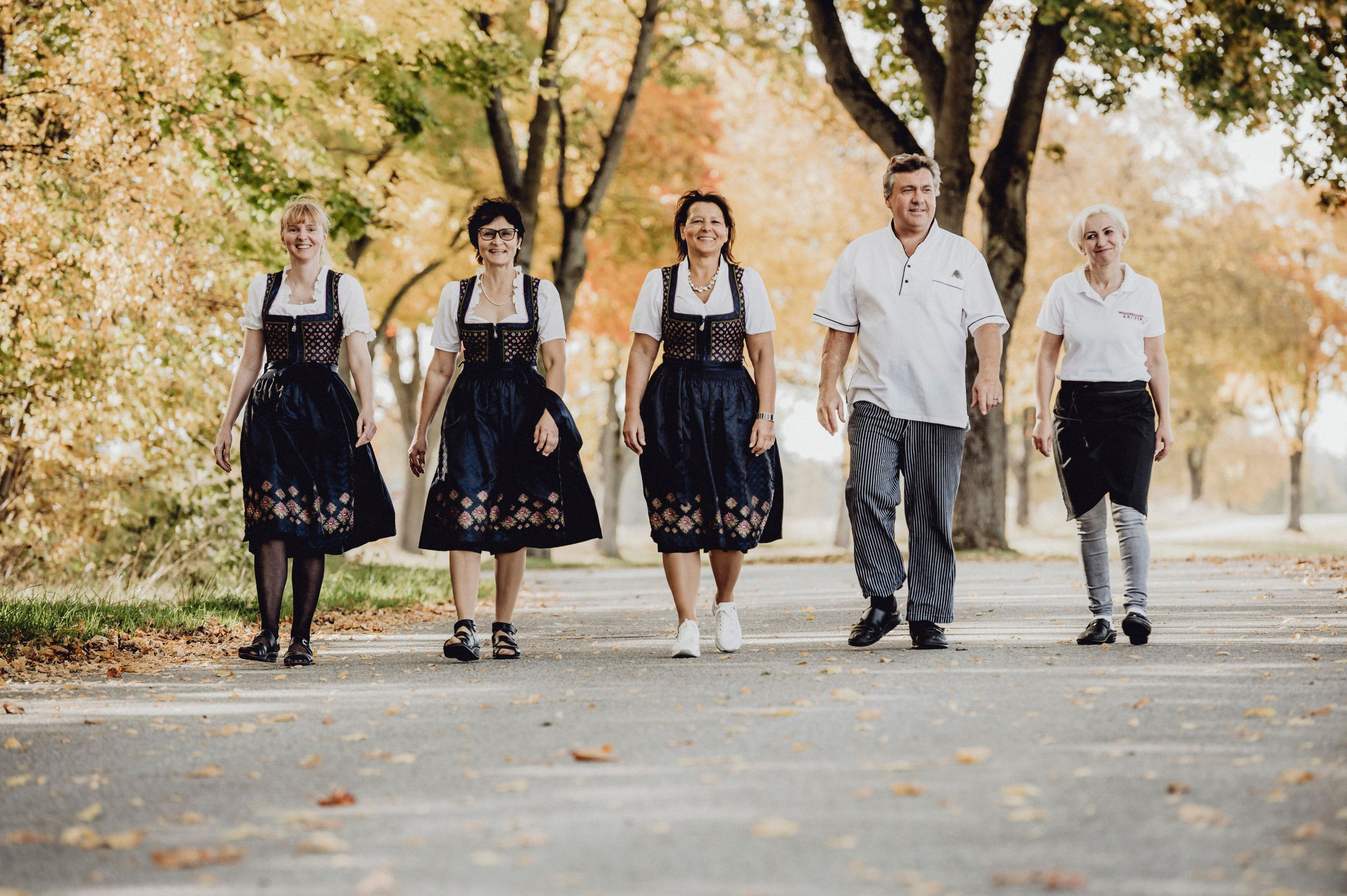 Five people in traditional dress walk along a tree-lined street.