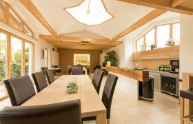 Interior view of a modern tasting room with wooden tables and chairs, large windows and a bar with bottles of wine.