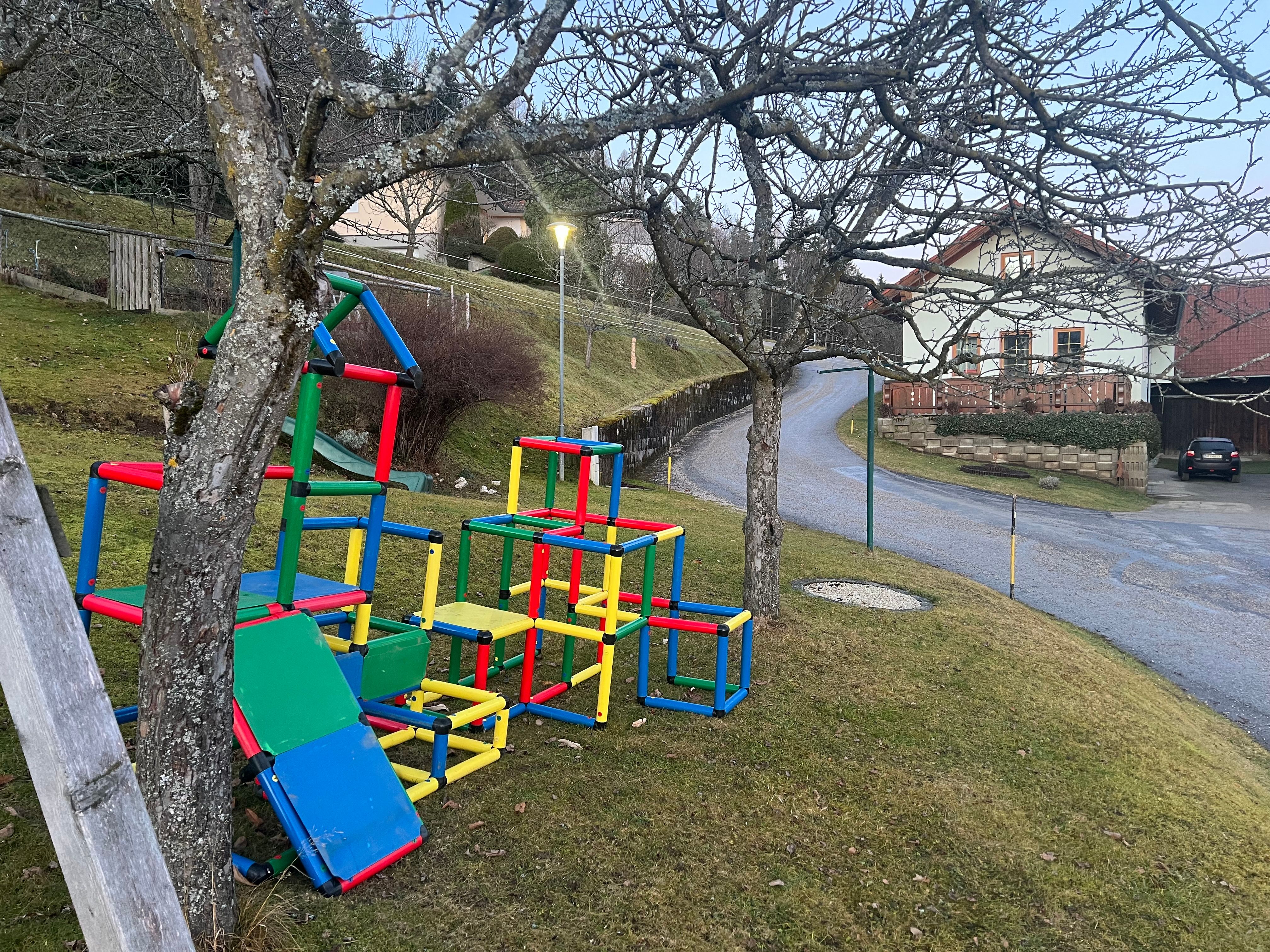 Colorful climbing playground with slide on a meadow next to a road and a house.