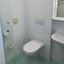 Small bathroom with white tiled walls, a toilet, washbasin and toilet roll holder.
