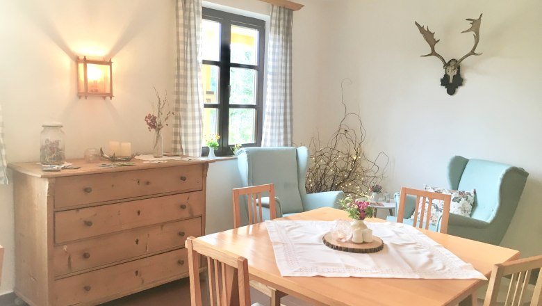 Cozy breakfast room with wooden table, chairs, chest of drawers and decorations.