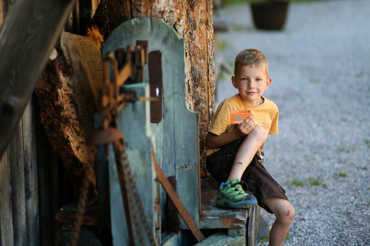 A boy sits on a wooden bench and holds the Wilde Wunder Card in his hand.