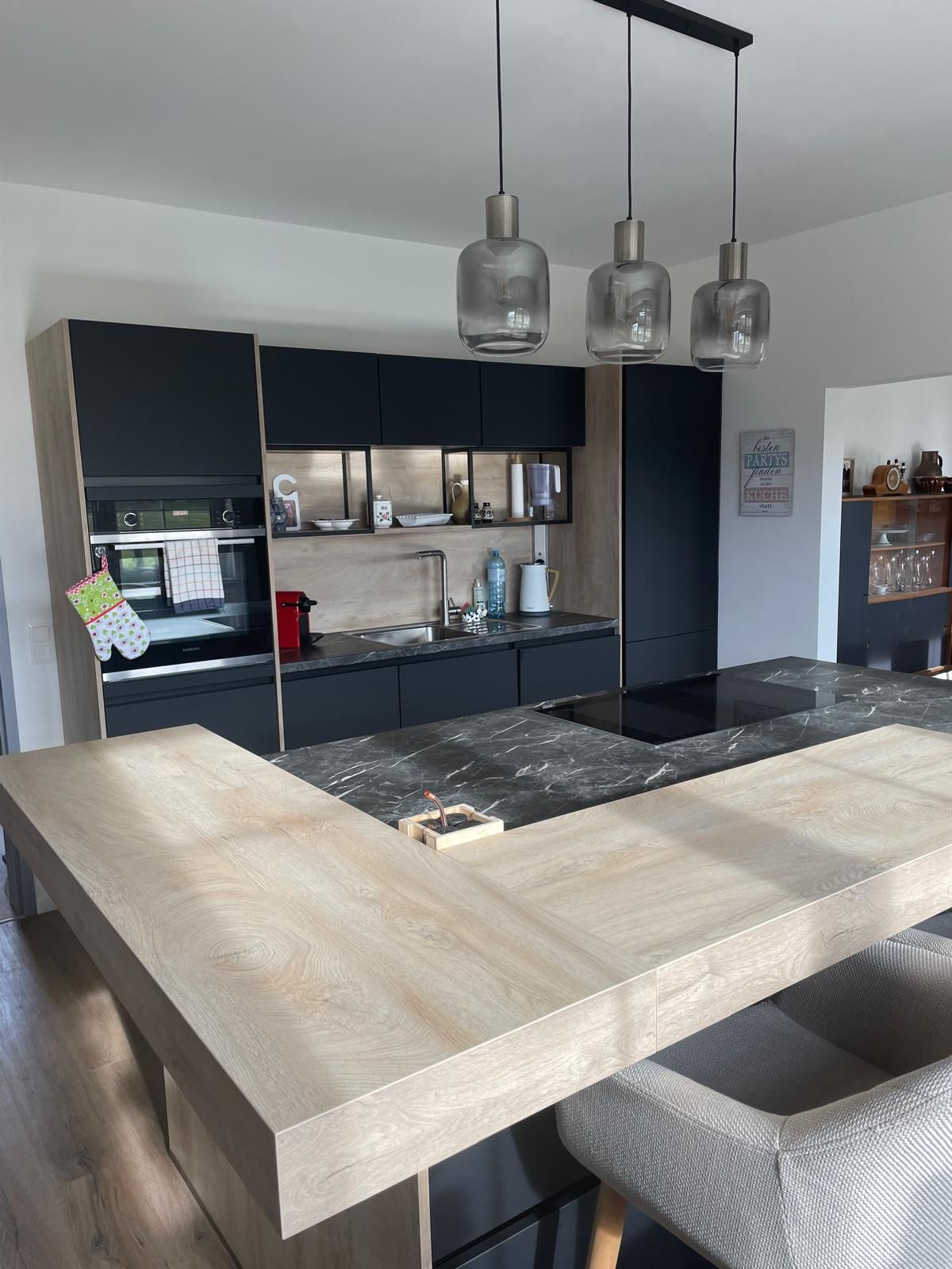 Modern kitchen with wood and marble elements, three hanging lamps and black cupboards.
