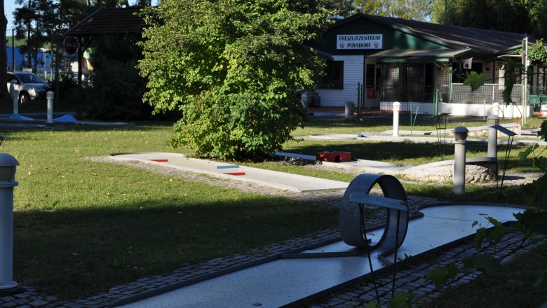 Miniature golf course with obstacles and a building in the background.