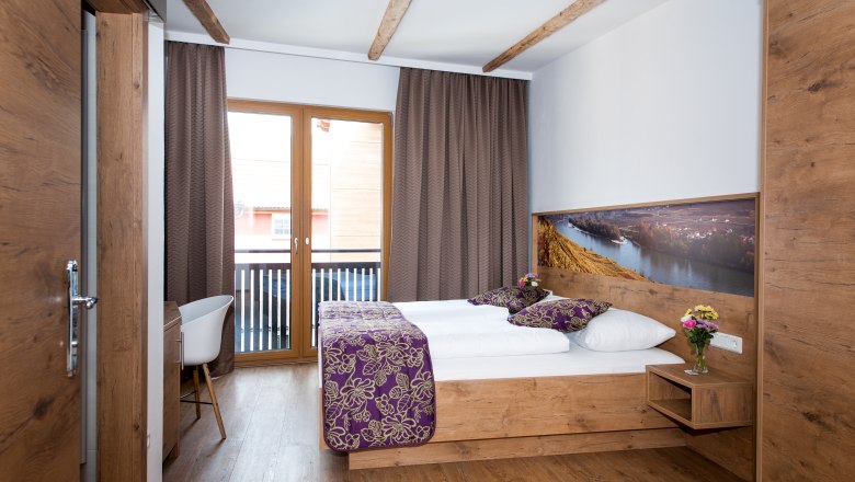 A cozy hotel room with wooden furniture, a double bed, balcony and decorative cushions.