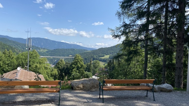 Two benches with a view of a mountain landscape and a bridge.