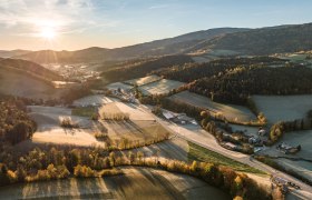 Aerial view of a rural landscape at sunrise with fields, forests and scattered buildings.