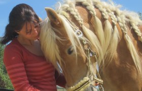 A woman in a red sweater stands next to a horse with a braided mane.