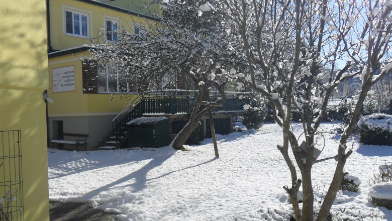 Winter scene with yellow building and snow-covered garden.
