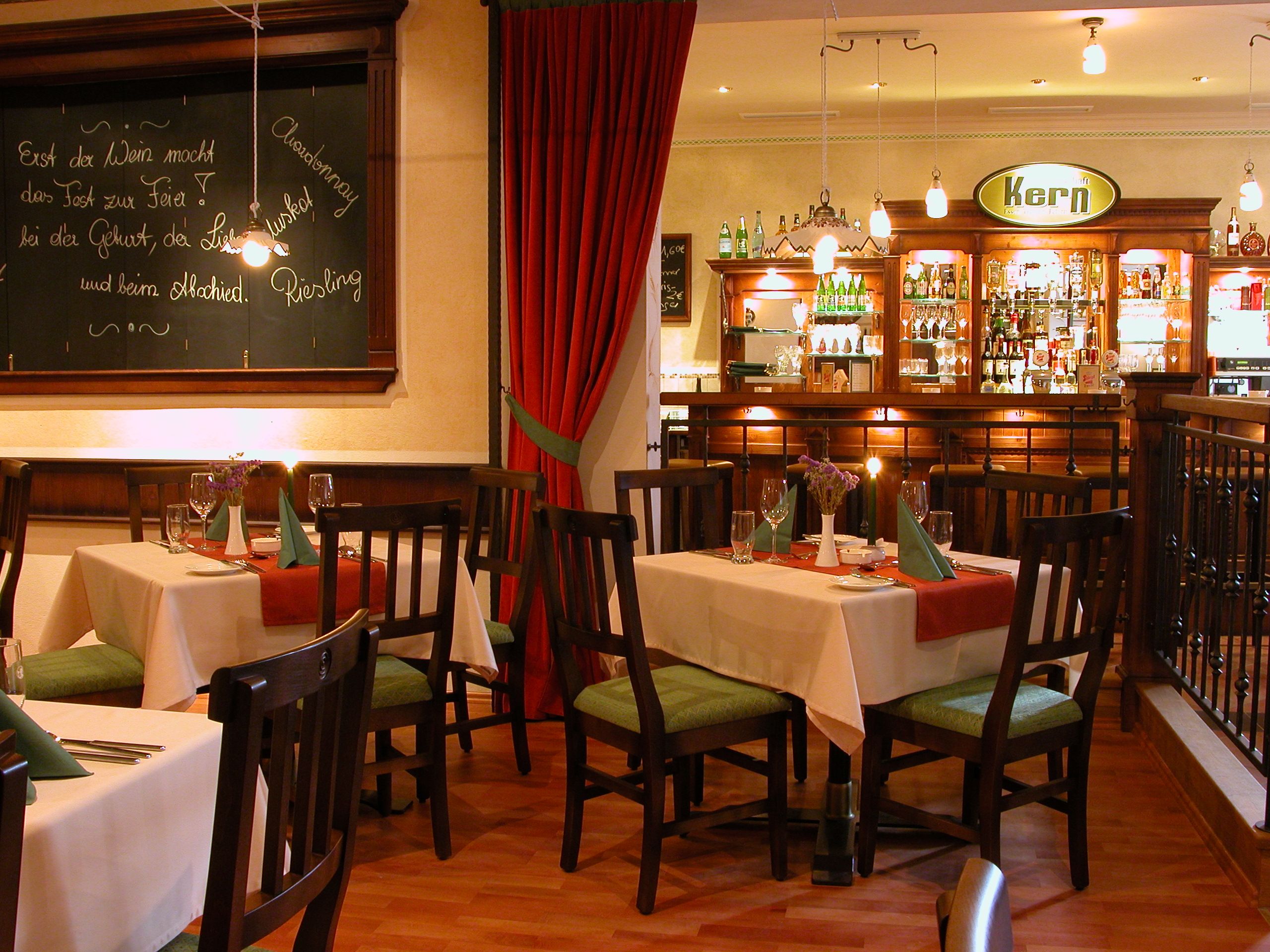 Cozy restaurant with wooden furniture, set tables and a bar in the background.