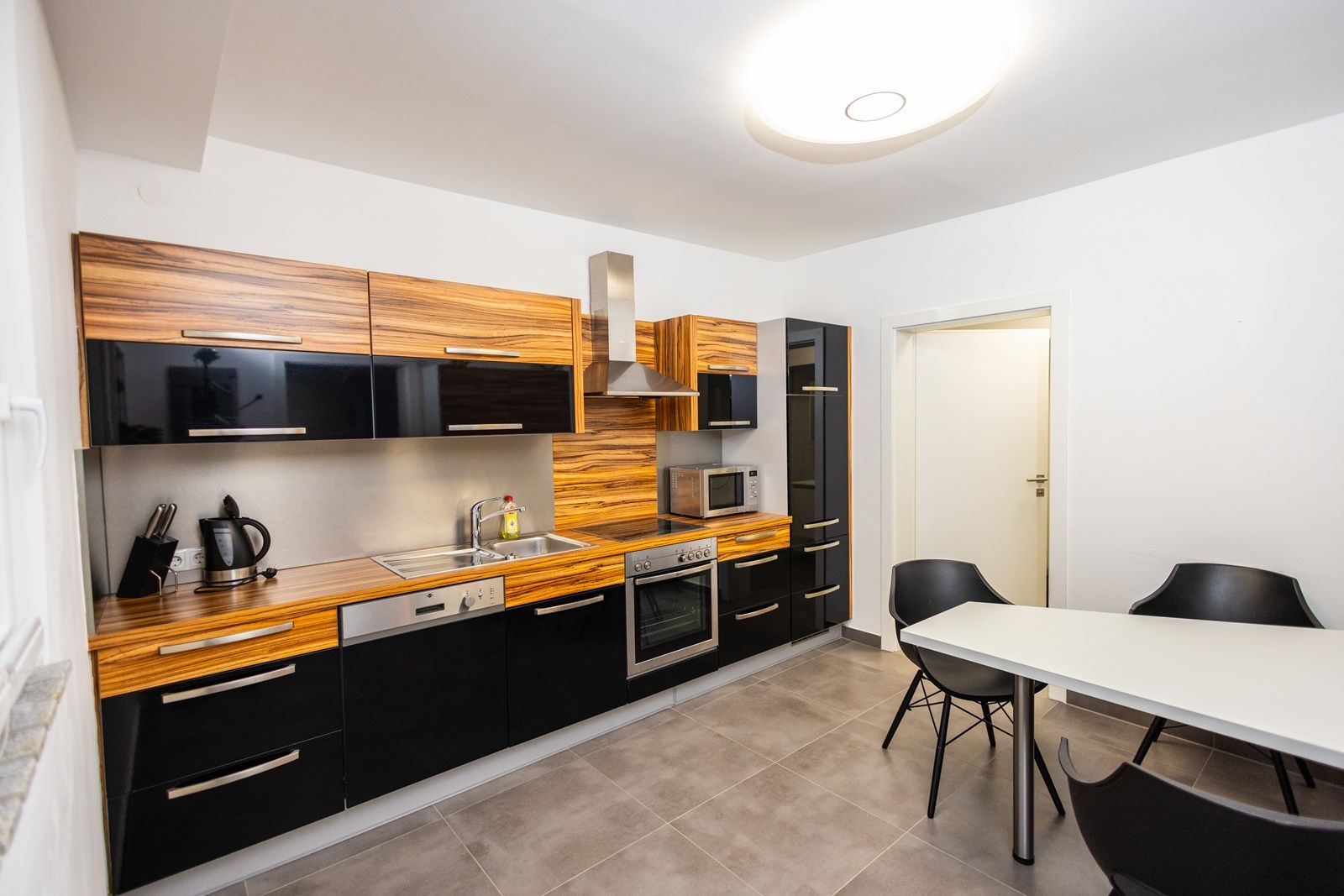 Modern kitchen with wooden and black high-gloss fronts, dining table and chairs.