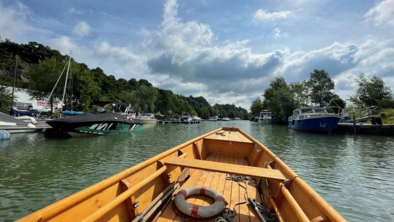 View from a wooden boat of a harbor with several boats and trees on the shore under a cloudy sky.