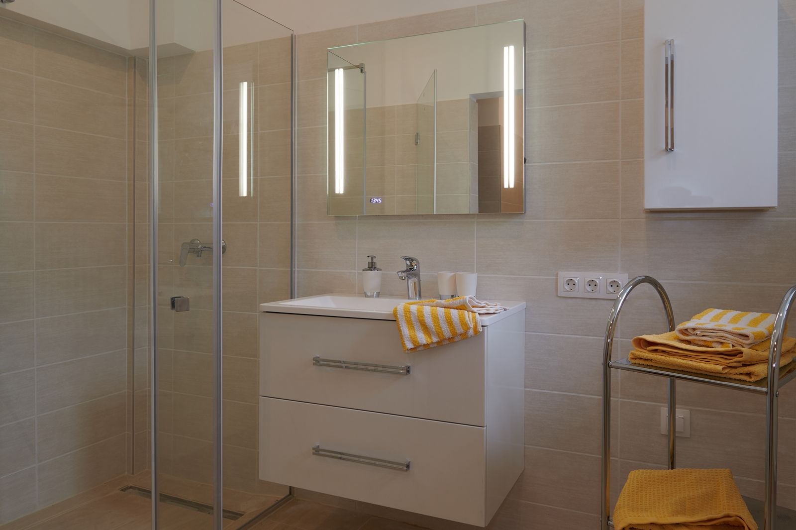 Modern bathroom with shower, washbasin and yellow towels.