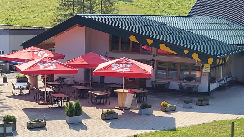 Exterior view of a restaurant with red parasols and outdoor seating.