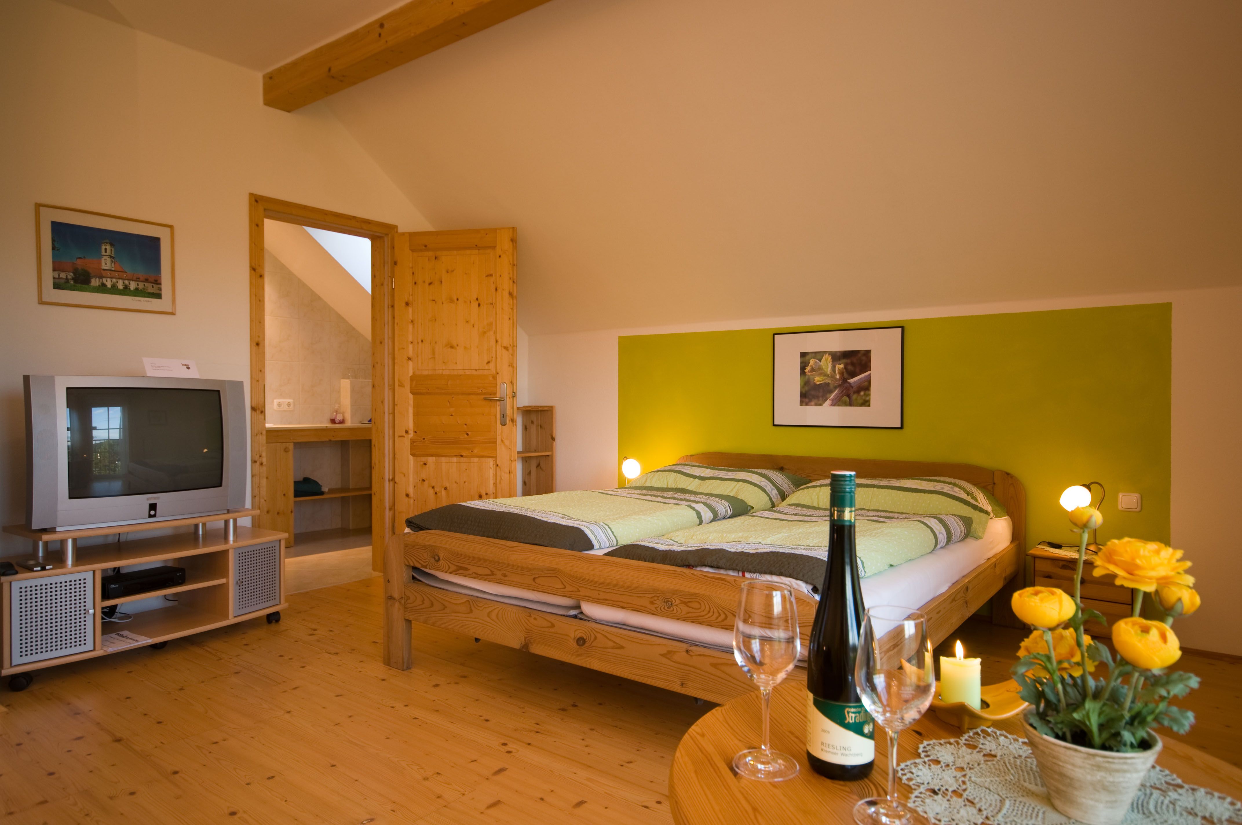 Cozy room with double bed, TV, bottle of wine and flowers on the table.