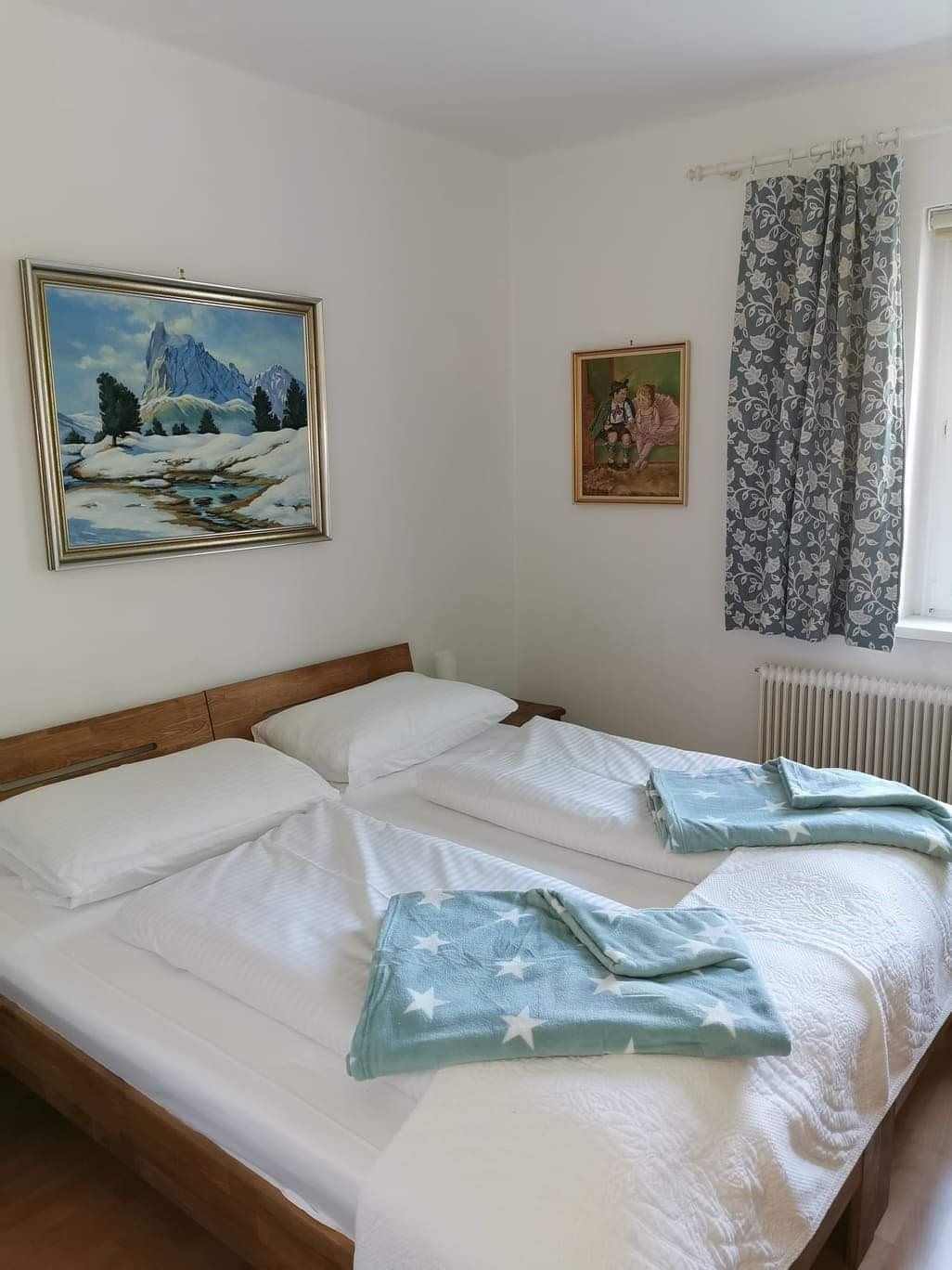 Bedroom with double bed, two pictures on the wall and a window with curtain.