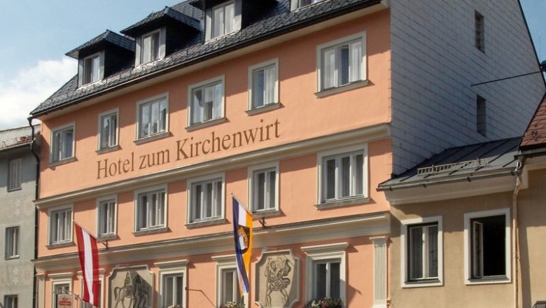 Hotel zum Kirchenwirt, © zVg Hotel zum Kirchenwirt Facade of the Hotel zum Kirchenwirt with flags and blue sky.