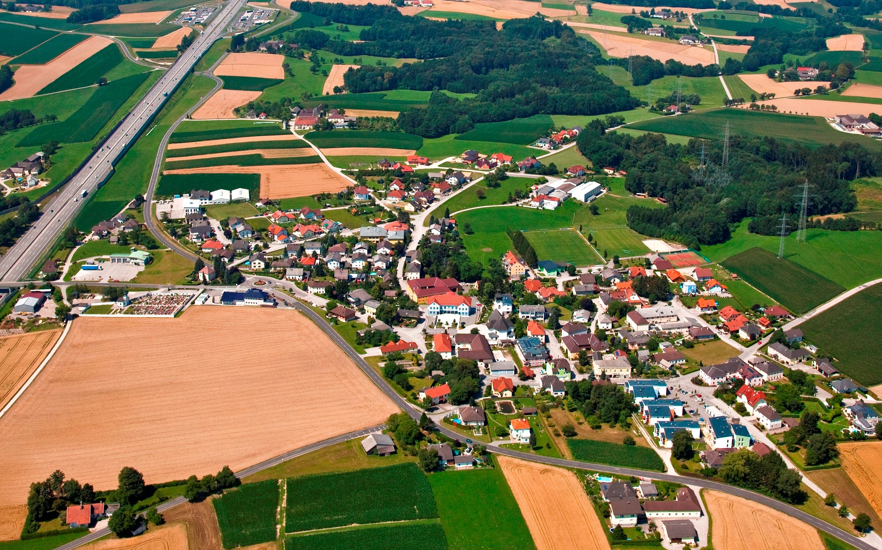 Aerial view of a village with fields and a highway.
