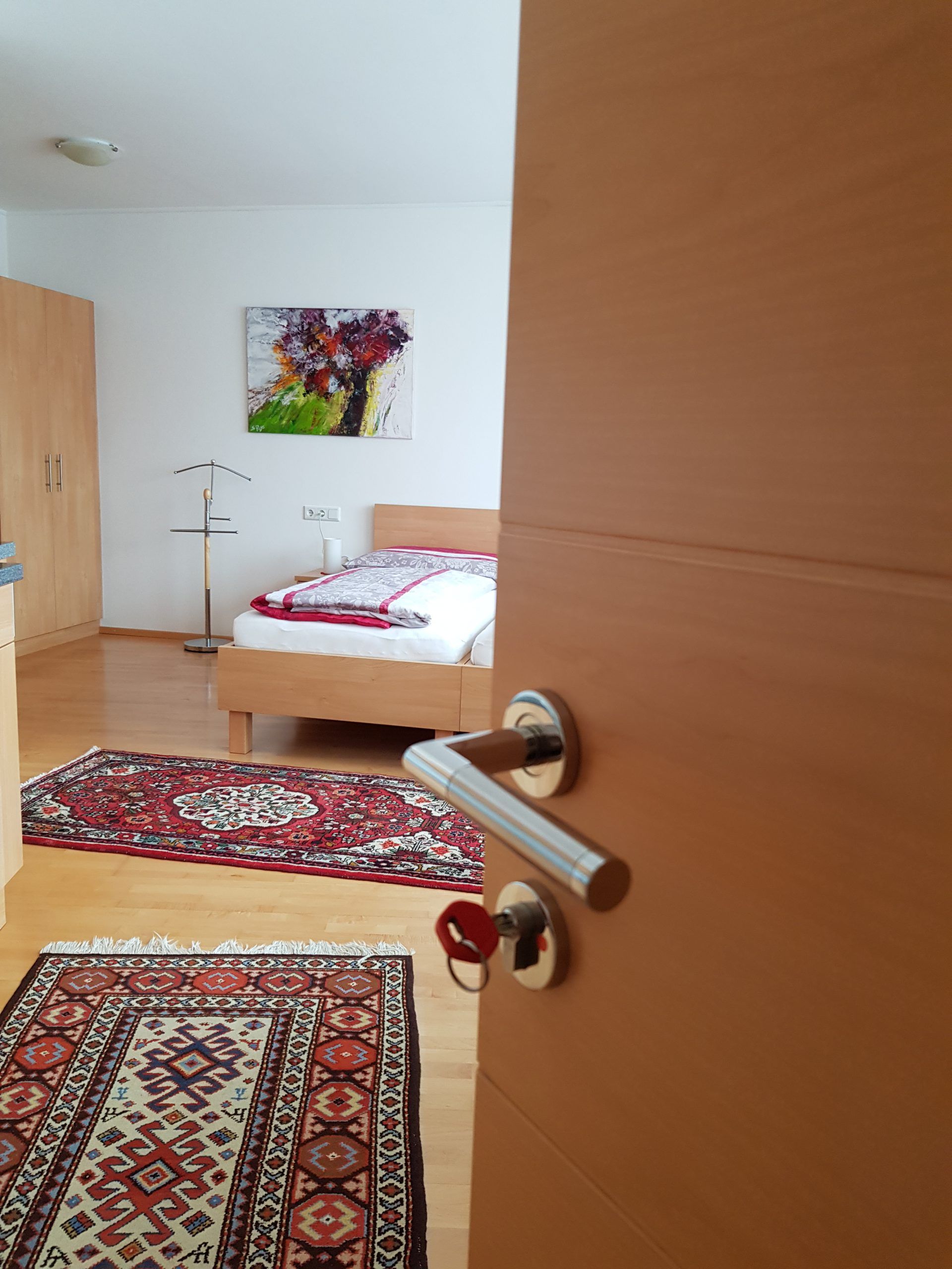 An open room with a bed, carpets and a painting on the wall.