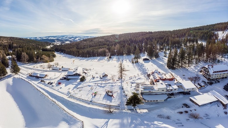 Aerial view of a snow-covered ski resort with buildings and forest in the background.