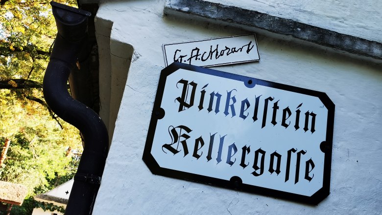 Sign with the inscription 'Pinkelstein Kellergasse' on a white wall.