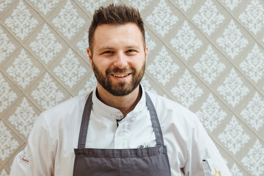 Philipp Essl in chef's clothes in front of a patterned wallpaper.