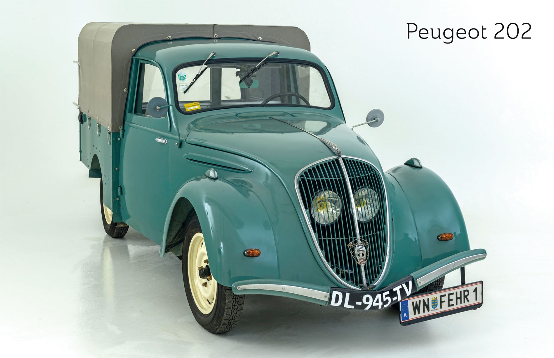 A green Peugeot 202 with tarpaulin, photographed from the front, on a white background.