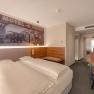 Modern hotel room with double bed, mural of an old motel, wooden furniture and desk.