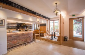 Interior view of a cozy wine bar with wooden furniture and brick counter.