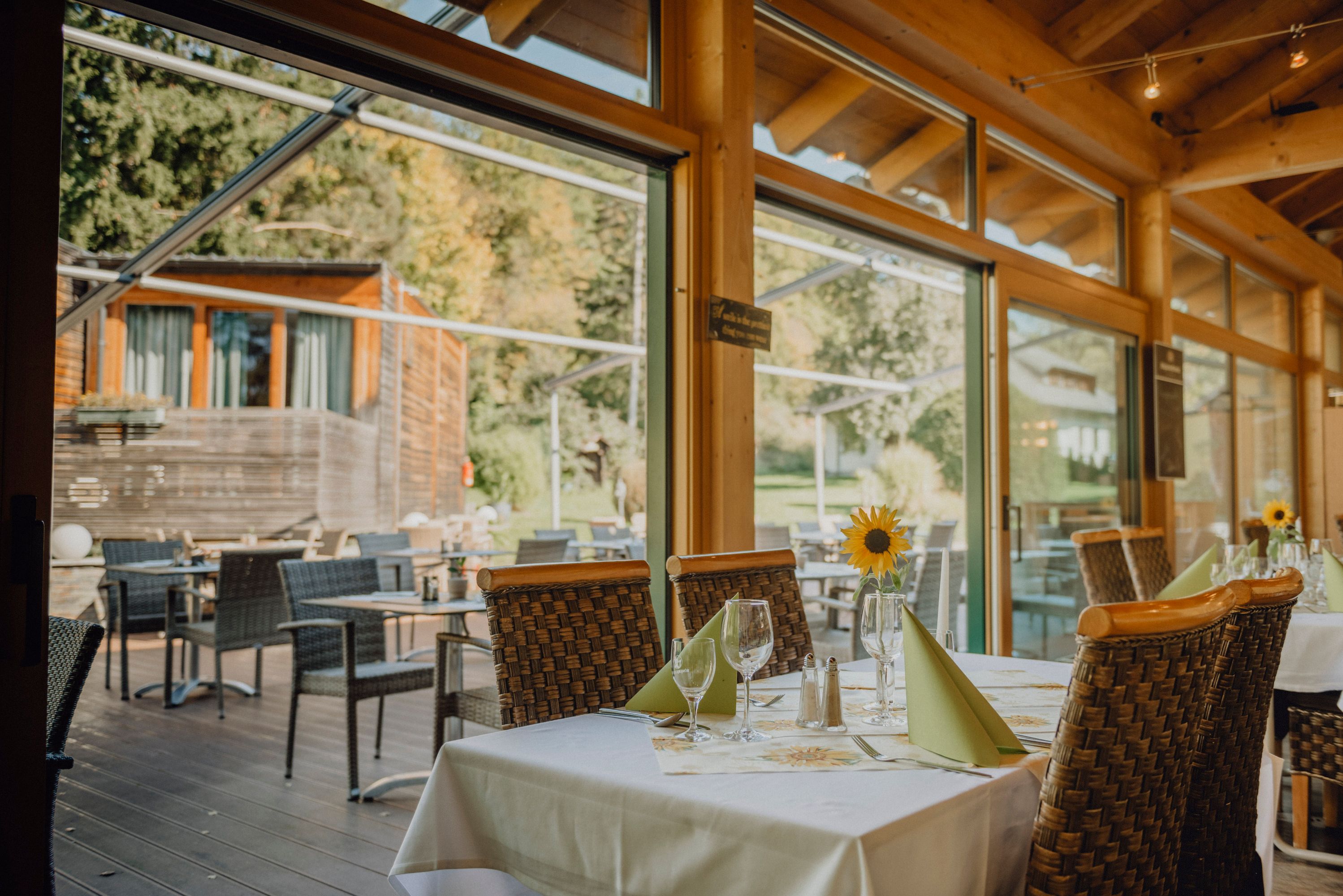 A restaurant with a winter garden and terrace, tables set with sunflowers and a view of the green surroundings.