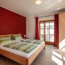 Bedroom with double bed, red wall and wooden furniture.
