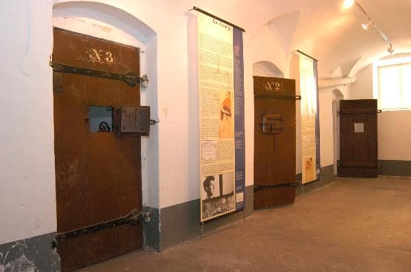 Three prison doors in a corridor with information boards on the walls.