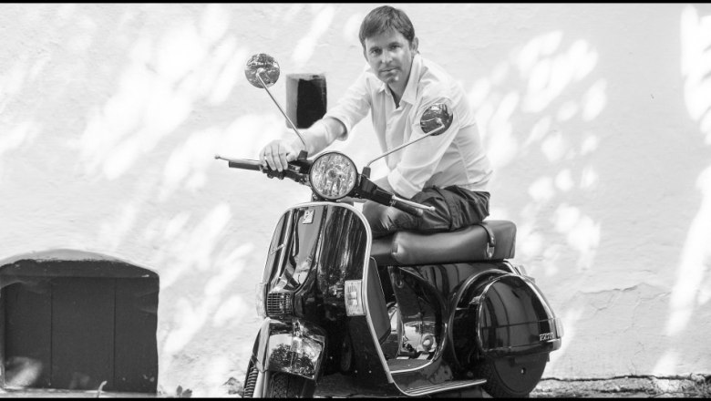Person on a Vespa in front of a white wall.