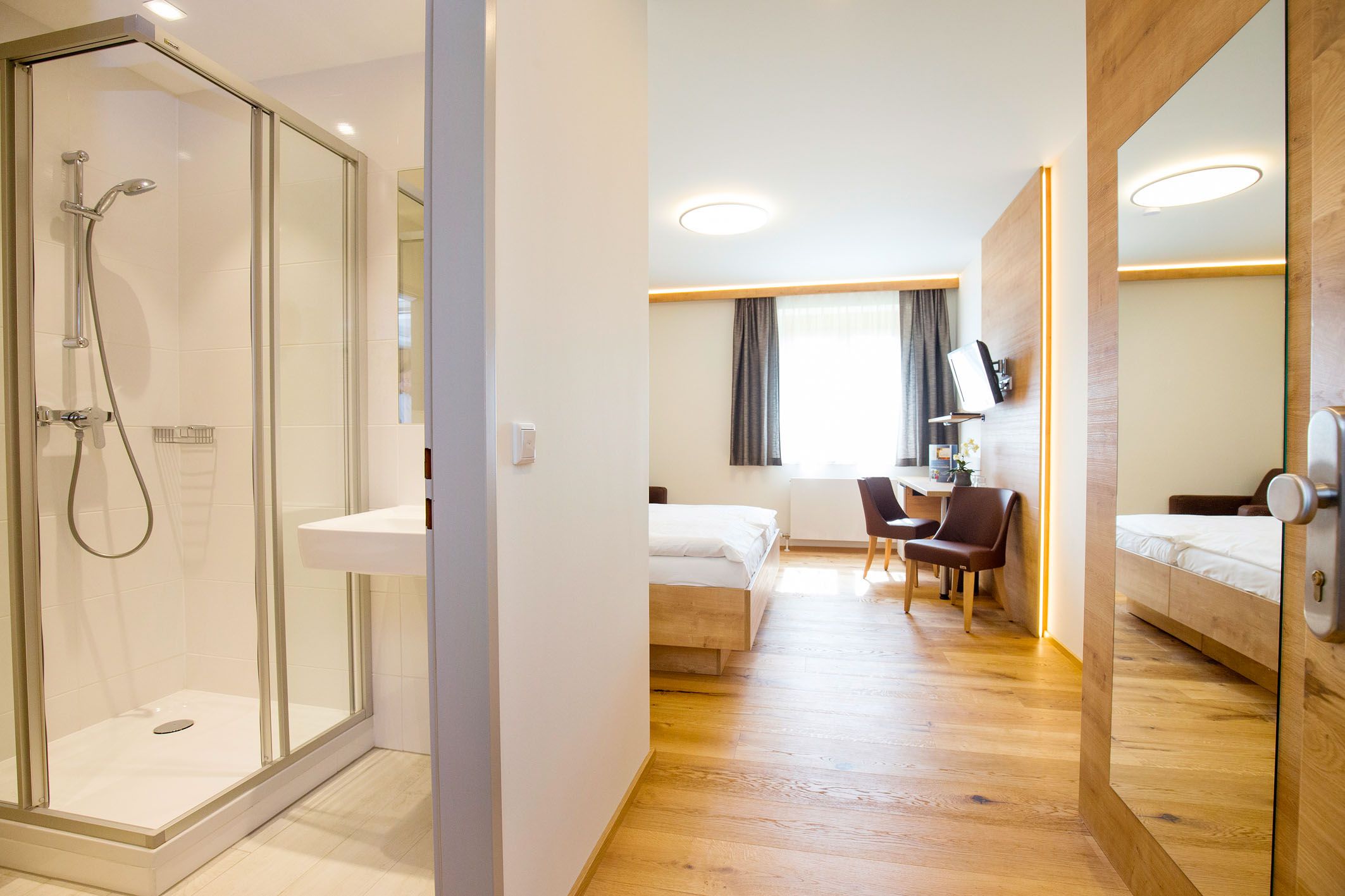 Modern hotel room with bathroom, bed, desk and chairs.
