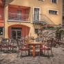 Outdoor area of a restaurant with tables and chairs on a paved courtyard, surrounded by flowers and plants.