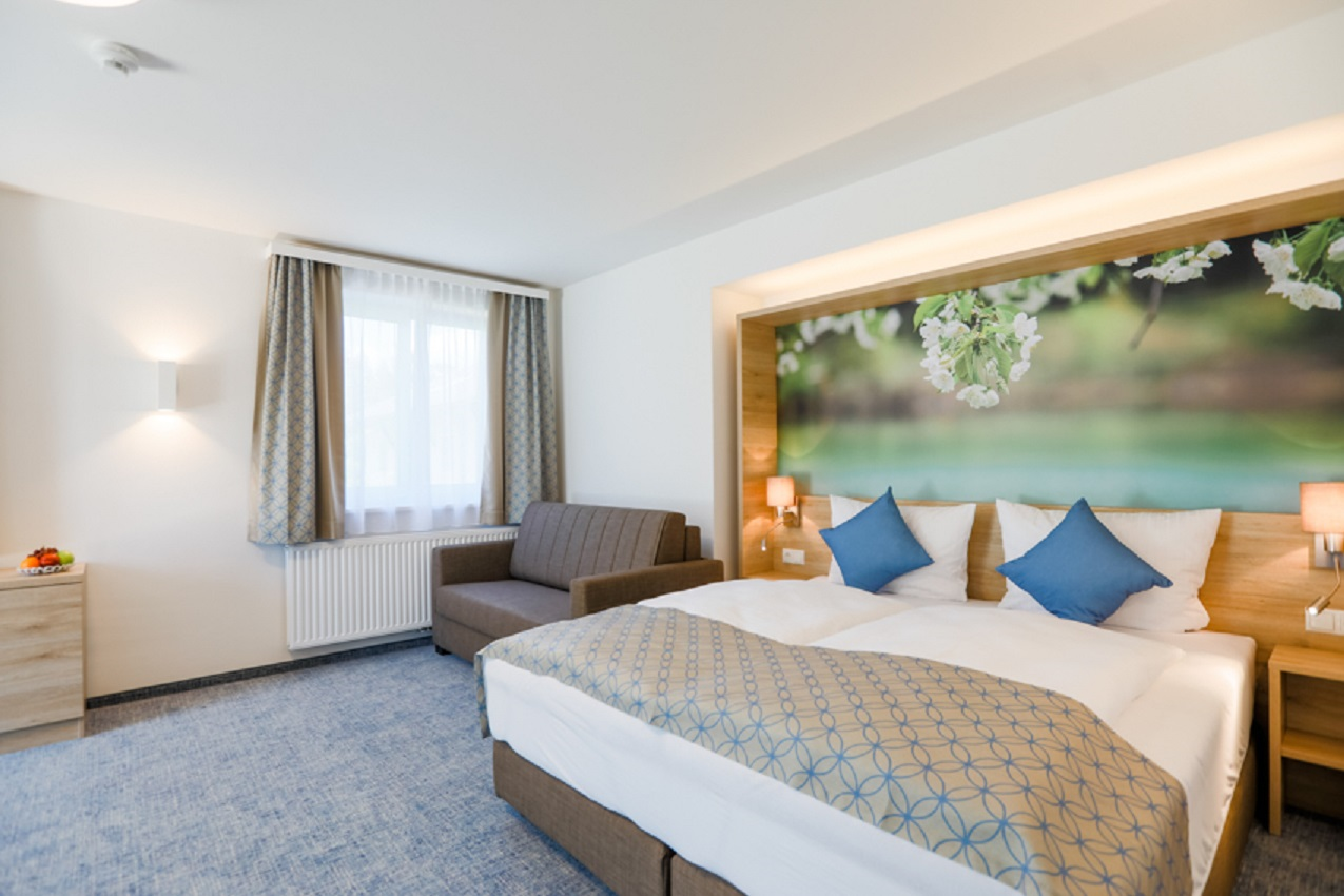 Modern hotel room with double bed, sofa and large mural with floral motif.