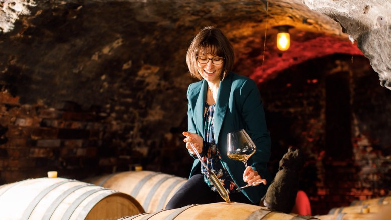 Woman tasting wine in the wine cellar with wine glass and barrel.