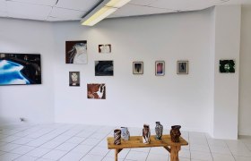 Gallery room with works of art on the wall and ceramics on a wooden table.