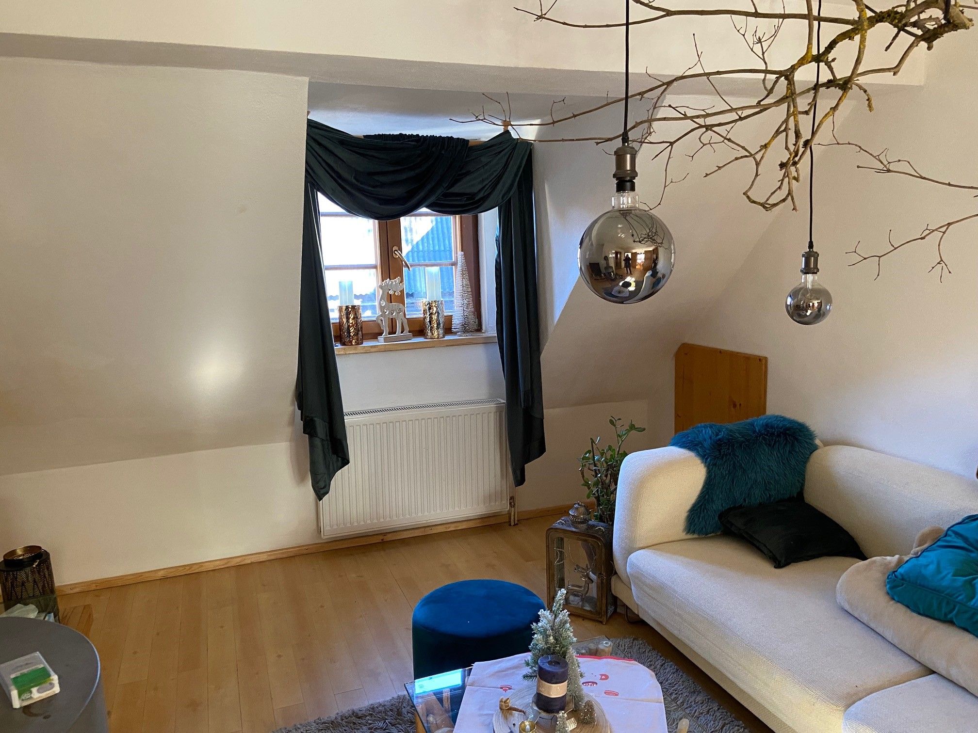 Cozy living room with sofa, wooden floor, windows with curtains, decorative candles and hanging lamps.