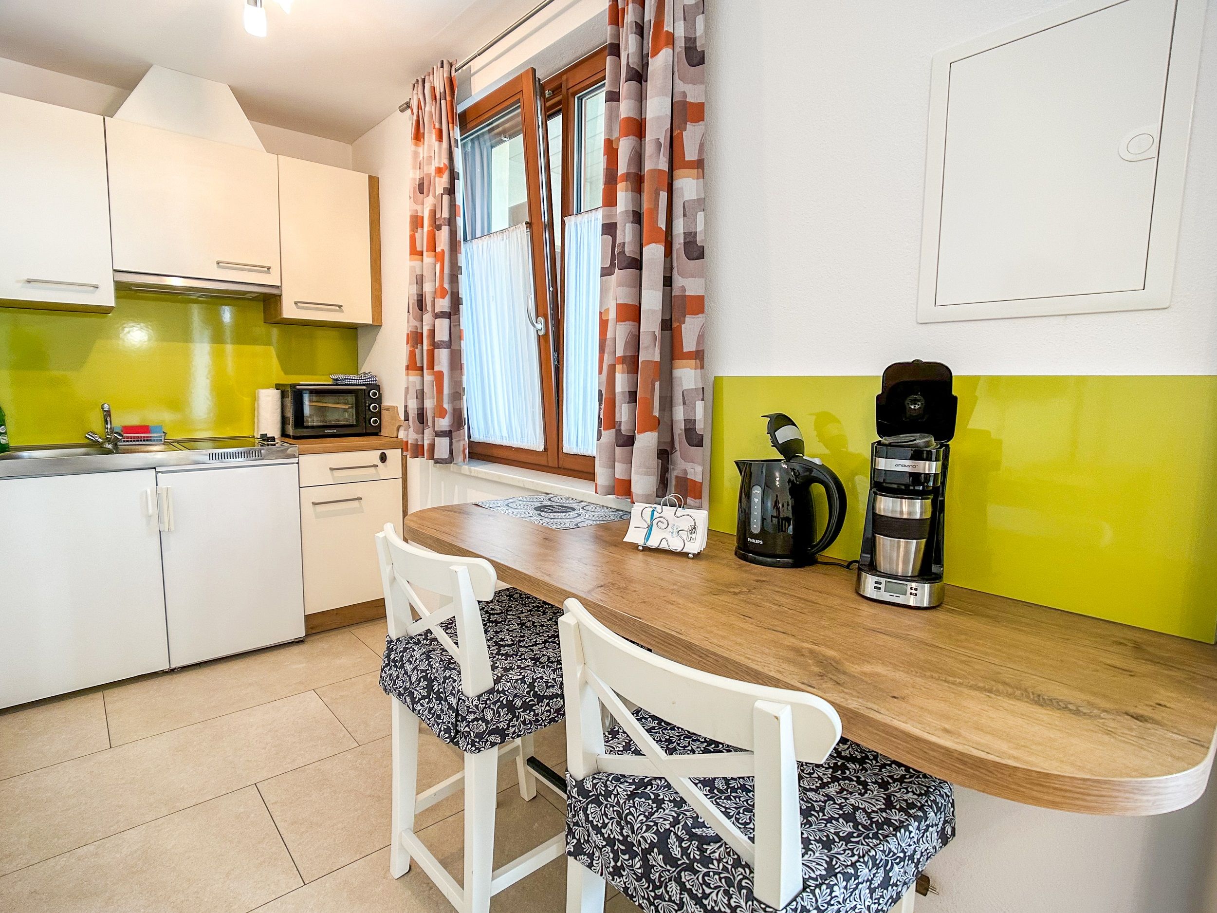Modern kitchen with green splashback, white cupboards, wooden counter and coffee machine.