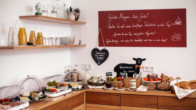 Breakfast buffet with juice, bread, cold cuts and fruit in a cozy room.