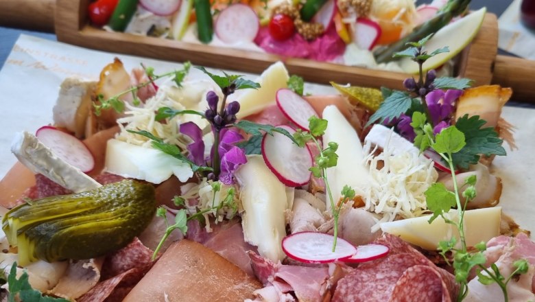 A Heurigen platter with various types of sausage and cheese, radishes, gherkins and herbs served on a wooden board.