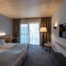 Modern hotel room with double bed, TV, floor lamp and balcony.