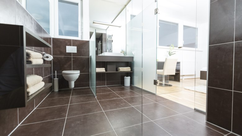 Modern bathroom with dark tiles, glass walls and white sanitary facilities.