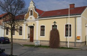Yellow building with the inscription 'Gemeindeamt', red roof, tree and lantern in front of it.