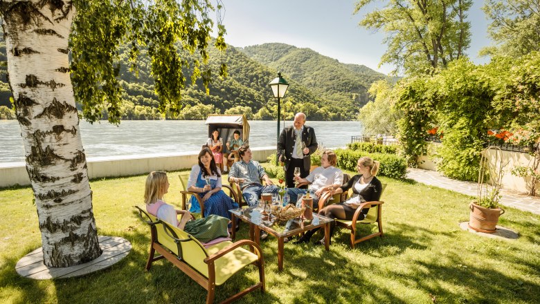 Group of people sitting in the garden of a restaurant on the riverbank.